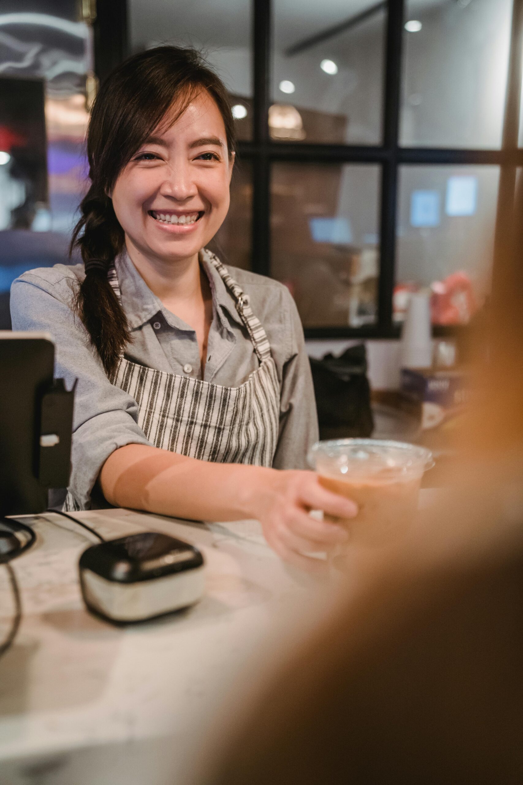 HOME Smiling barista serving coffee at a modern cafe counter.